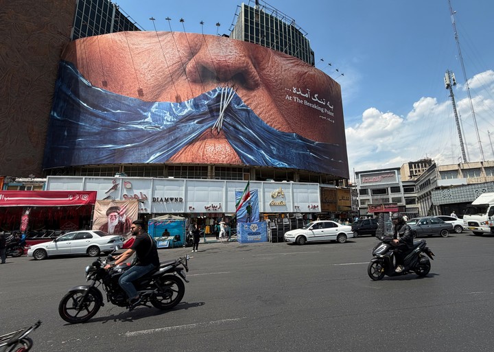 Vehículos circulan frente a una valla publicitaria que muestra el estrecho de Ormuz y los labios cosidos de Trump. Foto: AP